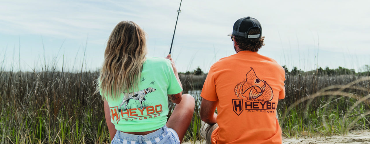 Man and woman in Heybo shirts, sitting in a marsh.